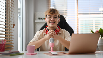 Man podcaster using laptop and microphone recording podcast from home studio