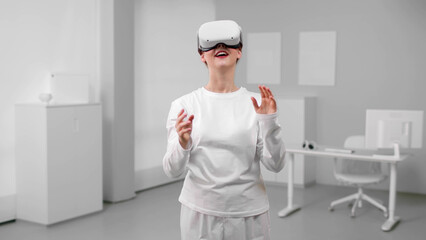 Beautiful young girl wearing virtual reality headset standing in white room
