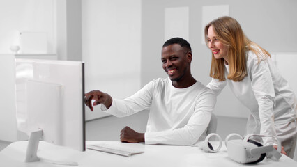 Multiethnic colleagues in white clothes discuss data on computer and smile working in white office