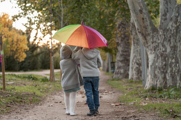 un par de amigos de excursión por un parque otoñal con un paraguas arco iris	