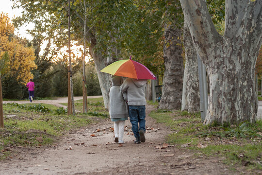 dos hermanos caminando por un bosque en oto&ntilde;o con un paraguas aco iris