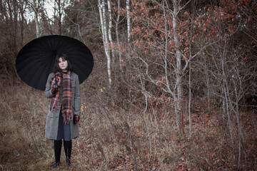 teenager girl with black umbrella in autumn forest