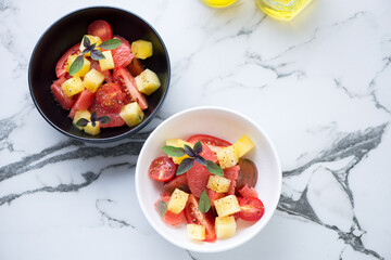 Salad with grapefruit, tomatoes and yellow watermelon served in two bowls on a white marble background, high angle view, horizontal shot with copyspace