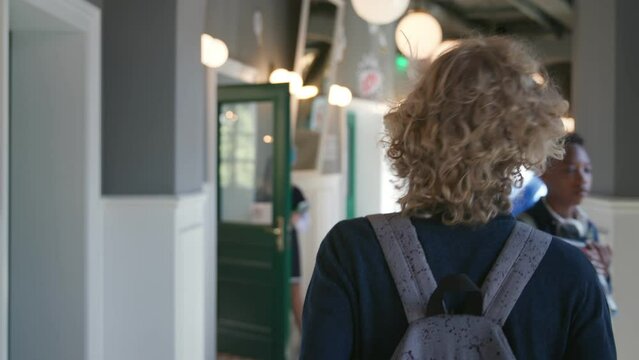 Back view of teenage boy with backpack walk in school corridor looking for classroom