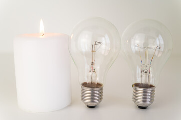 Candle with burning flame, next to unlit bulbs. Energy saving and rationing. Increase in tariffs and energy crisis.
