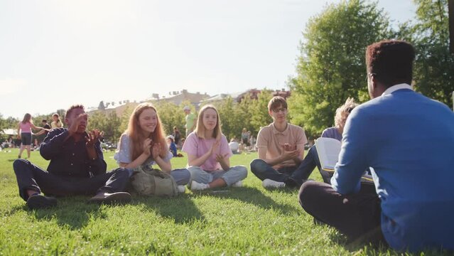 High school students sit on glass and applaud to teacher having outdoor lesson