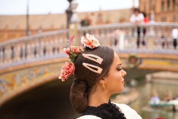 Detail of head with flowers and hairpins of a beautiful teenage flamenco dancer with brown hair and dressed in dance clothes in a square in seville. Flamenco cultural heritage of humanity. - obrazy, fototapety, plakaty