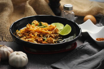 Pad Thai or Fried noodle Thai style, Thai style served with lime and seasonings. In a black palette, the visual style is dark tones.