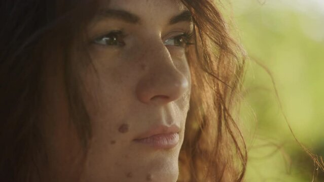 Handheld close up catching sunbeam on curly caucasian woman face with freckles and birthmarks outside
