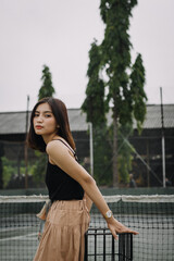 Beautiful female model, wearing a black tanktop, posing and stylish in the middle of a tennis court in the afternoon.
