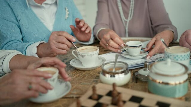 Close-up of senior friends sitting indoors in cafe drinking coffee or tea together.