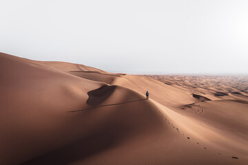 Fototapeta na wymiar Man walking in the huge red desert dunes