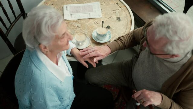 Happy senior couple sitting indoors in cafe drinking coffee or tea, laughing and having nice time together.