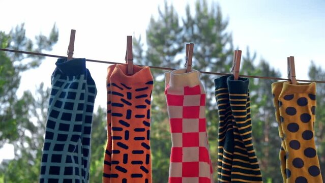 against the background of the sky and trees on the balcony, colorful bright men's socks with different patterns attached with wooden clothespins are drying on a rope in pairs. close-up. slow motion.