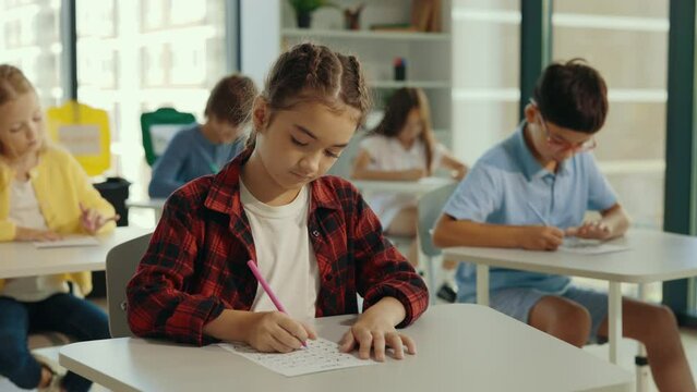 Exam in elementary school. Female beautiful pupil sits at a first desk in the classroom and fills out tests thinks about answers. Education children.