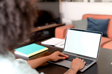 Female student using laptop for watching webinars, lectures, sits at desk in home office and taking notes, eastern woman taking a part in online educational course, researching topic, copy space