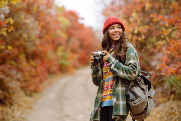 Fototapeta na wymiar Beautiful woman taking pictures in the autumn forest. Smiling woman enjoying autumn weather. Rest, relaxation, lifestyle concept.