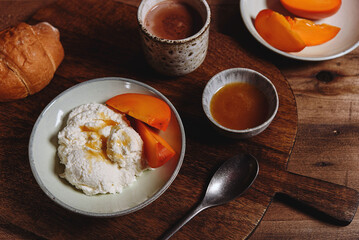 Homemade ricotta cheese or cheese curd served with fresh persimmon and honey and croissante on wooden background. Healthy breakfast. Haze effect. Selective focus