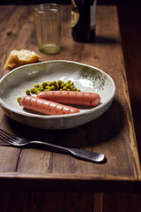 Grilled sausages with green peas served with dark beer and artisan bread on wooden table. Bachelor's dinner. Selective focus