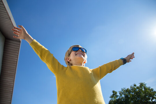 joyful boy in yellow sweater, sunglasses spread his arms against of blue sky and sun. victory, success, joyful emotions, happiness, freedom, positive thinking. happy childhood concept. Bright future