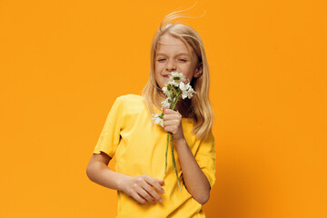 a beautiful cute girl of school age stands with a bouquet of daisies in her hands on an orange background and the wind blows her blond hair. studio photography