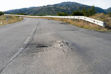 Broken spot in middle of road stretching in wild area on sunny summer day. Deformed asphalt caused...