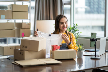 Small business entrepreneur SME concept.Female online seller sells a clothes via online marketplace platform.Asian female clothes shop owner folding a t-shirt and packing in a cardboard parcel box.