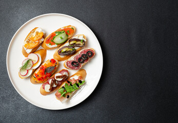 Brushetta, antipasti  or authentic traditional spanish tapas set on white plate. Variety of  pinchos (pintxos) in a bar or restaurant or home party or picnic. Flat lay, top view, copy space for text