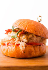 Burger with chicken fillet, pineapple, arugula, tomatoes, bacon and sauce on a wooden plate on a white background