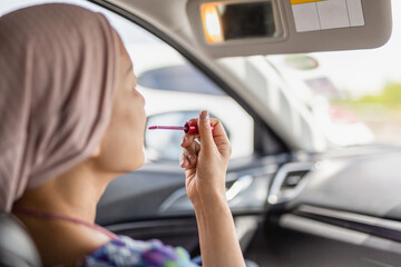 Woman looking in rear view mirror painting her lips doing applying make up in car.