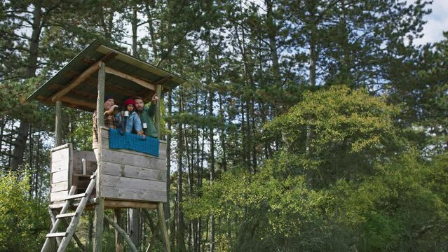 Grandfather, father and son having men time together in forest, sitting at high hunter seat drinking tea and observing nature.