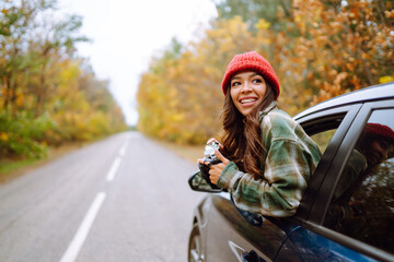 Beautiful woman takes pictures on the camerafrom the car window. Smiling woman enjoying autumn...