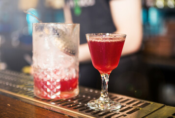 On the bar counter there is a mixing glass with the remnants of a cocktail and a ready-made cocktail in a glass