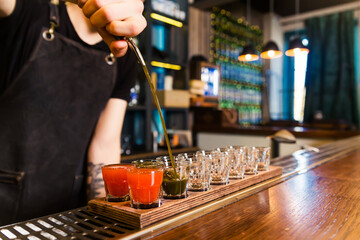 The bartender at the bar pours red tincture into shots