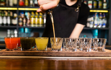 The bartender at the bar pours red tincture into shots
