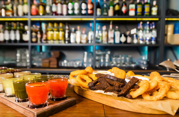 On the bar counter there is a set of various tinctures and a plate with snacks - onion rings, cheese sticks, balls and croutons