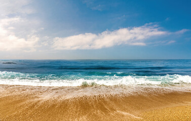 Beautiful seascape with turquoise water turning into a blue sky with spindrift clouds, light waves with white lambs roll onto shore golden beach.