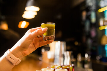 A woman hand holding a glass shot with a green alcoholic drink. Alcohol consumption