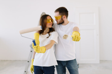 Portrait of a married man and woman in yellow safety glasses and gloves who have moved into a new house and are doing repairs on a isolated background. Couple renovates the interior using paint roller