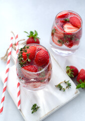 Detox strawberry thyme infused water or mocktail in a glass on the white wood board with white background