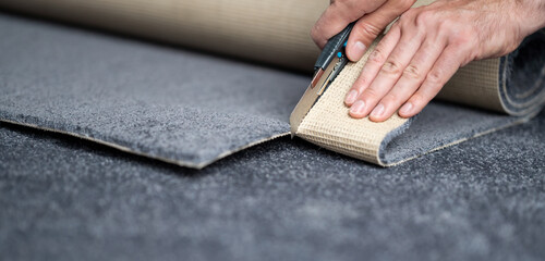 Handyman cutting a new carpet with a carpet cutter. - obrazy, fototapety, plakaty