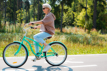 Senior older elderly modern woman rides a bicycle in a city park in the forest. Active pensioner,...