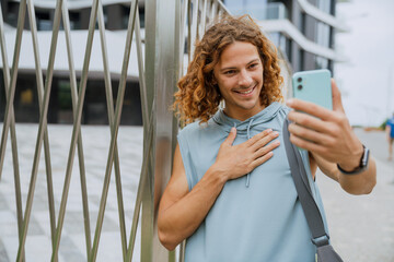 Portrait of young long-haired athletic smiling man taking selfie