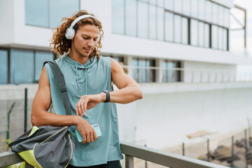 Young long-haired athletic man in headphones with bag and phone