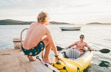 Father with teenager son on the bright yellow inflatable kayak returning back from evening ride by the Adriatic sea harbor in Croatia near from Sibenik city. Vacation and family values vertical image.