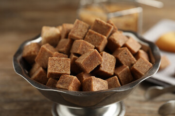 Brown sugar cubes in metal bowl on wooden table, closeup
