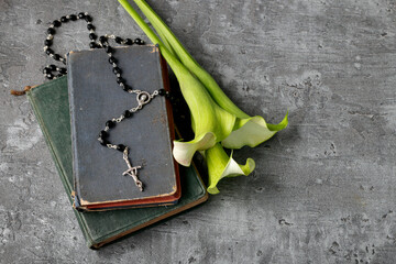 White calla flowers (Zantedeschia), rosary and Holy Bible on stone background.