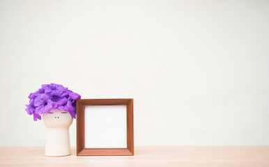 Purple bouquet in a white vase with a frame on a wooden shelf on a white wall background.
