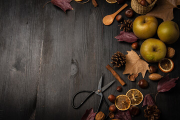 Top view of apples, nuts, oranges, cinnamon, scissors and autumn leaves, on a dark wooden background, horizontal, with copy space