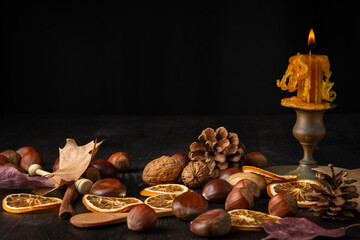 Close-up of lit orange candle, nuts and autumn leaves, on black background, selective focus, horizontal, with copy space